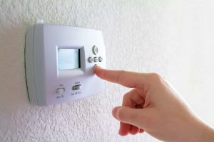 A person pushing a button on a wall-mounted thermostat